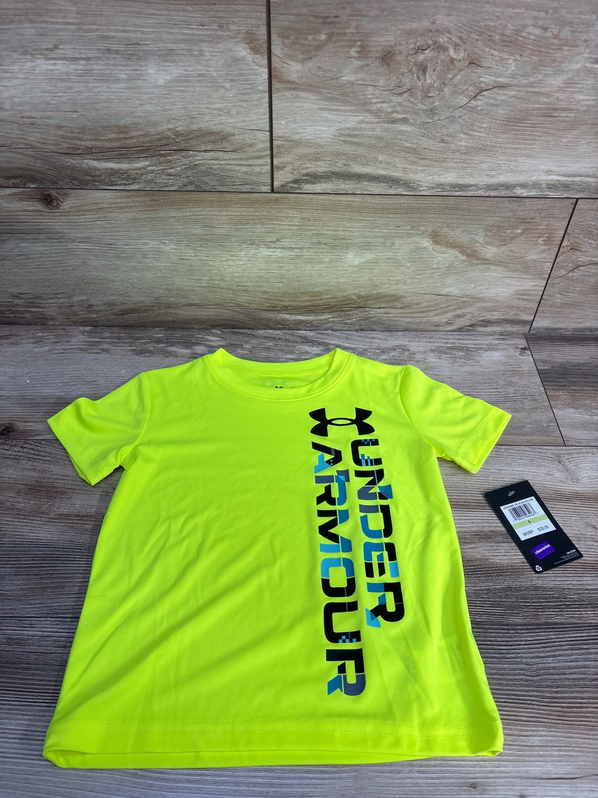 Flat lay of lime green Under Armour short-sleeve shirt with vertical UNDER ARMOUR logo and tag on wood background