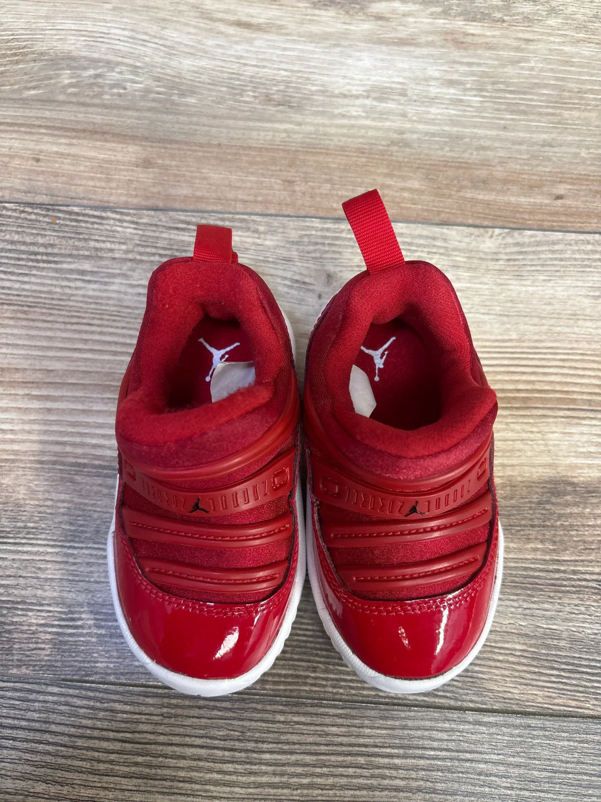 Top view of Air Jordan 11 Retro Little Flex TD Gym Red sneakers showing red uppers, white soles and slip-on closure on wood-grain surface