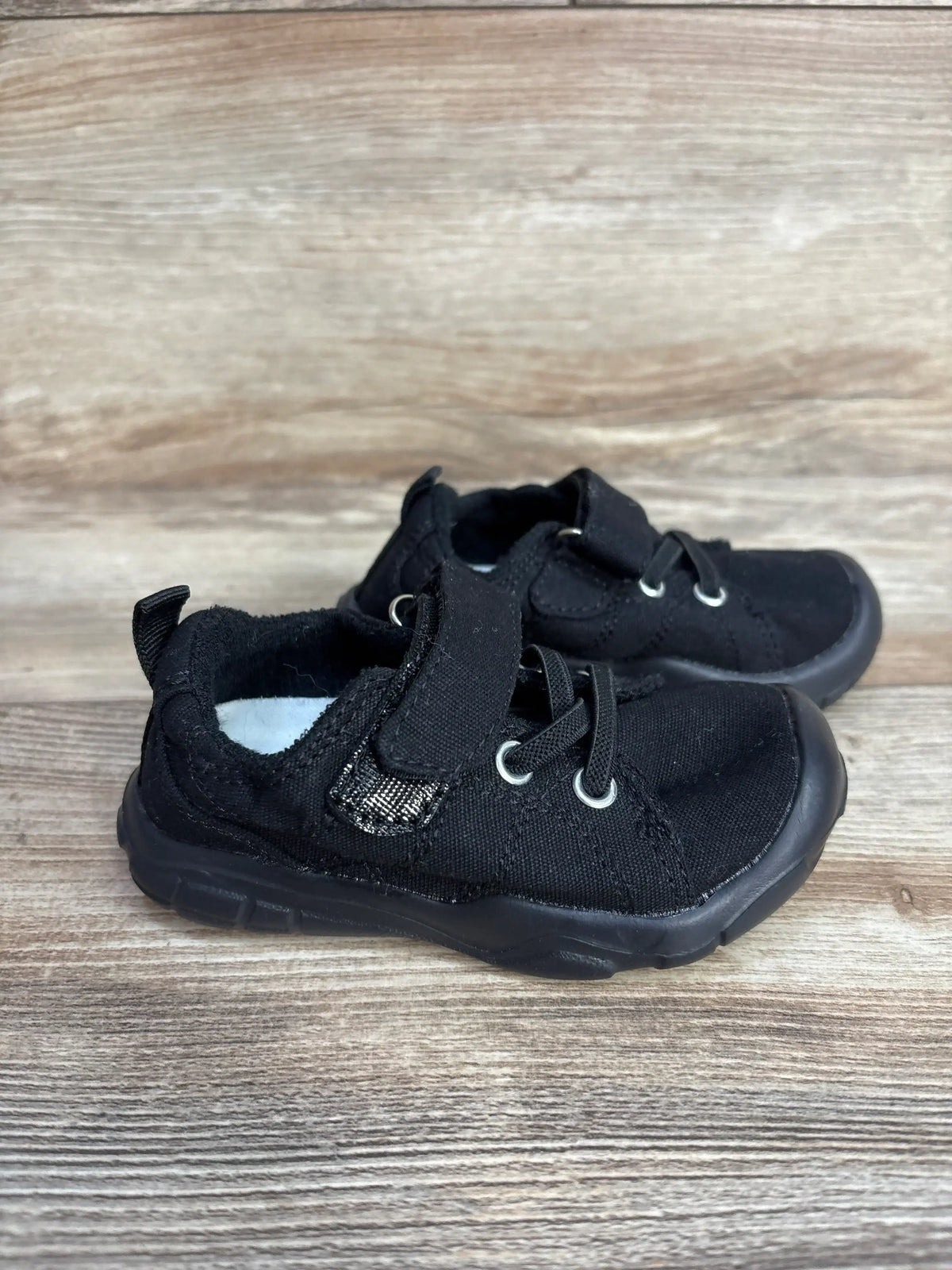 Pair of black toddler shoes with velcro straps on wooden surface