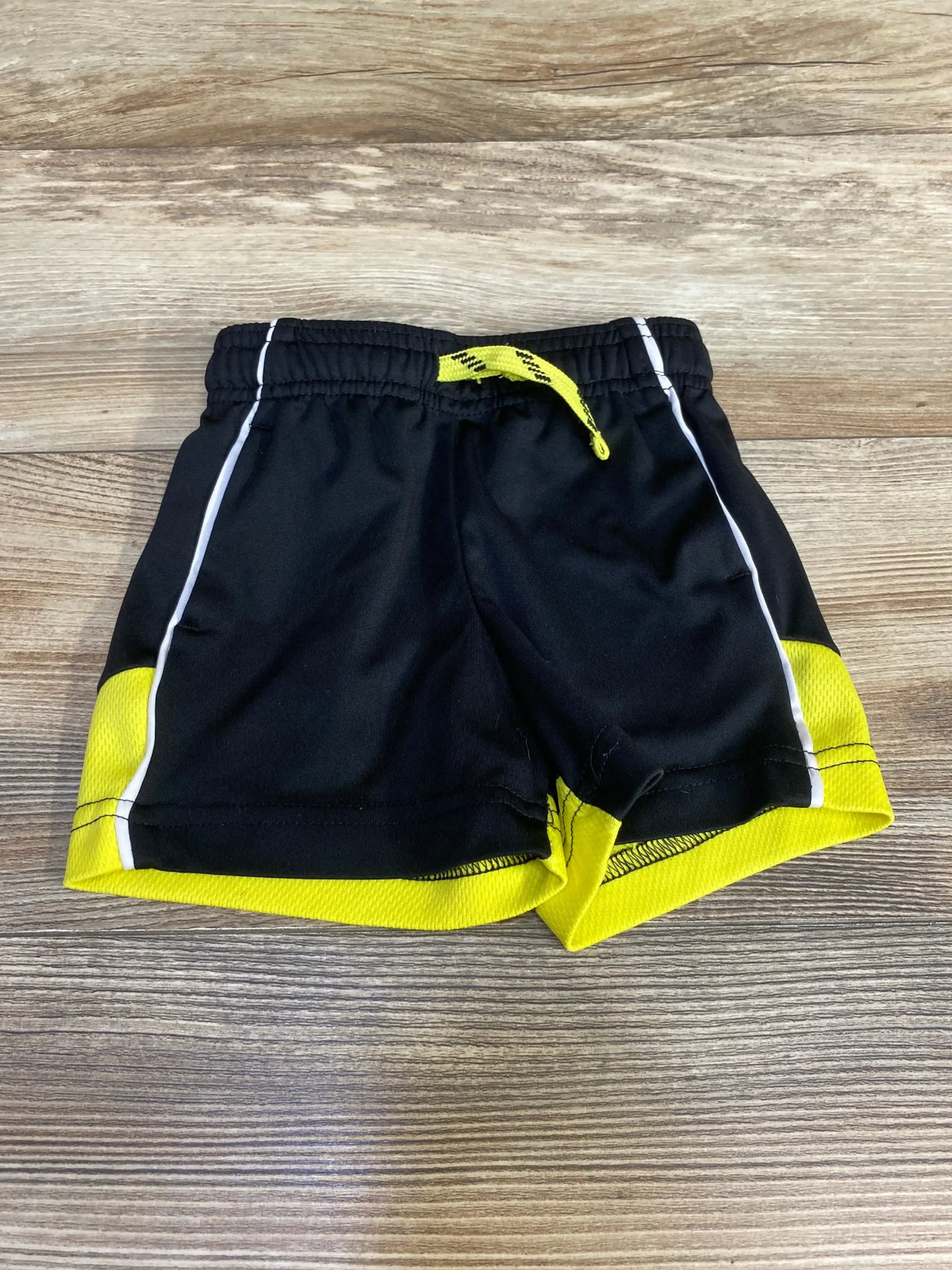 Front view of Jumping Beans toddler black drawstring active shorts showcasing yellow hem and drawstring on wood floor background