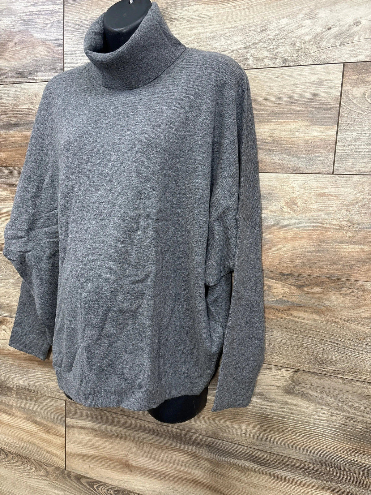 Grey turtleneck sweater displayed on black mannequin against wood panel background