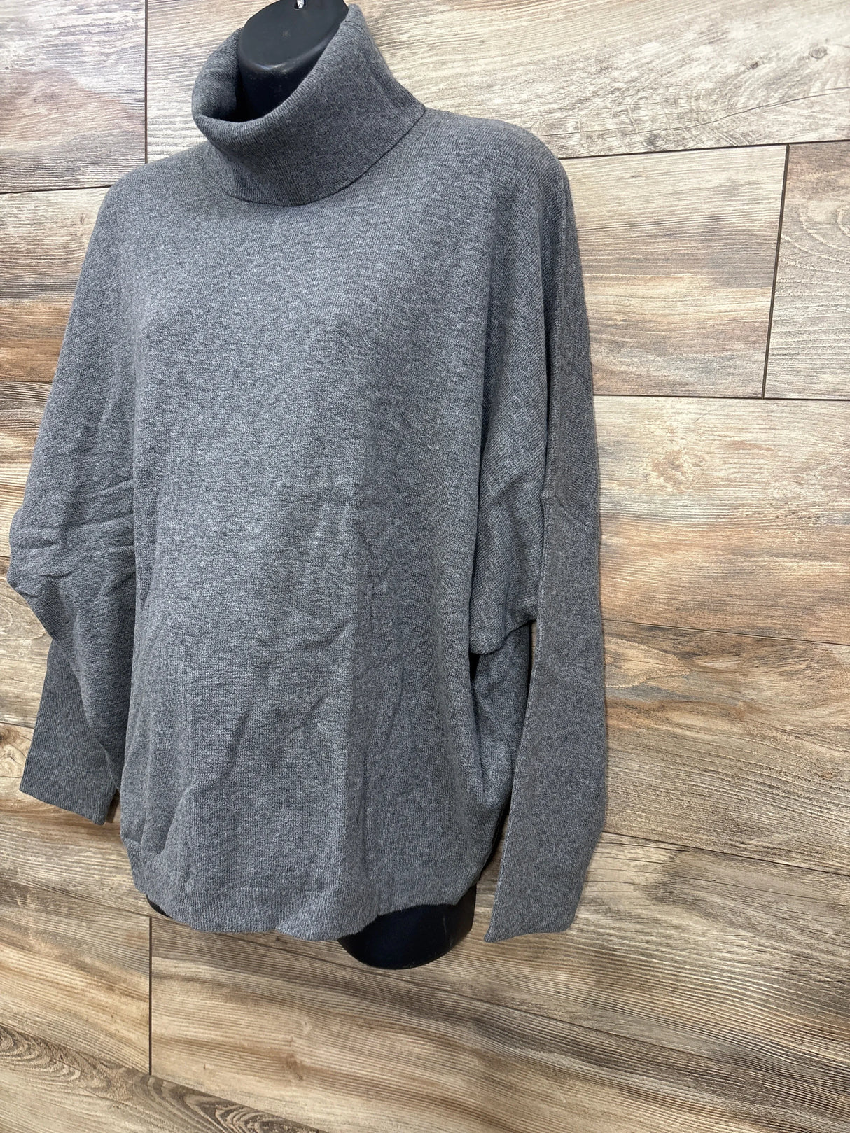 Grey turtleneck sweater displayed on black mannequin against wood panel background