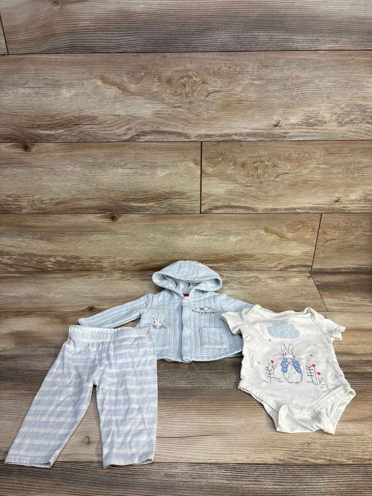 Peter Rabbit baby outfit set with striped hoodie, pants, and onesie on wood floor