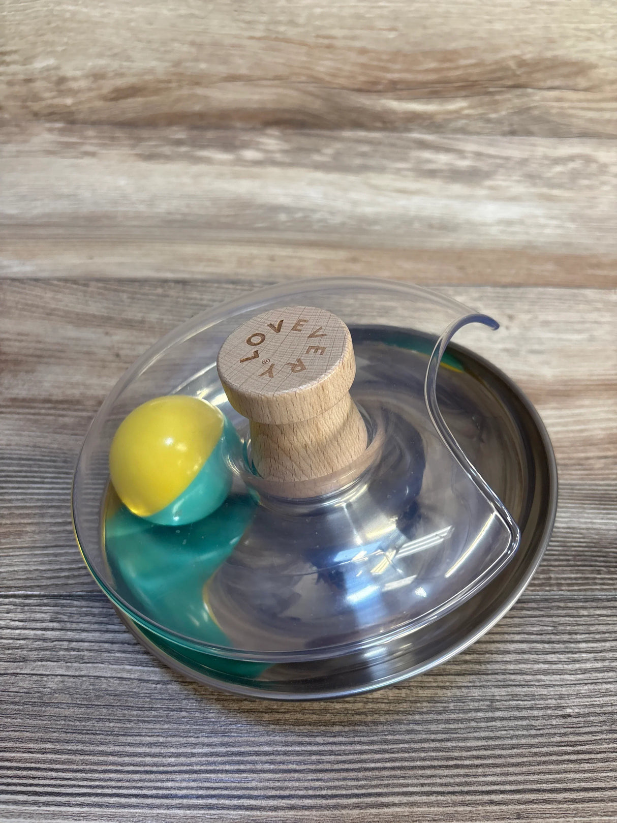 LOVEVERY wooden baby toy with yellow and teal ball in clear spinner base on wood surface