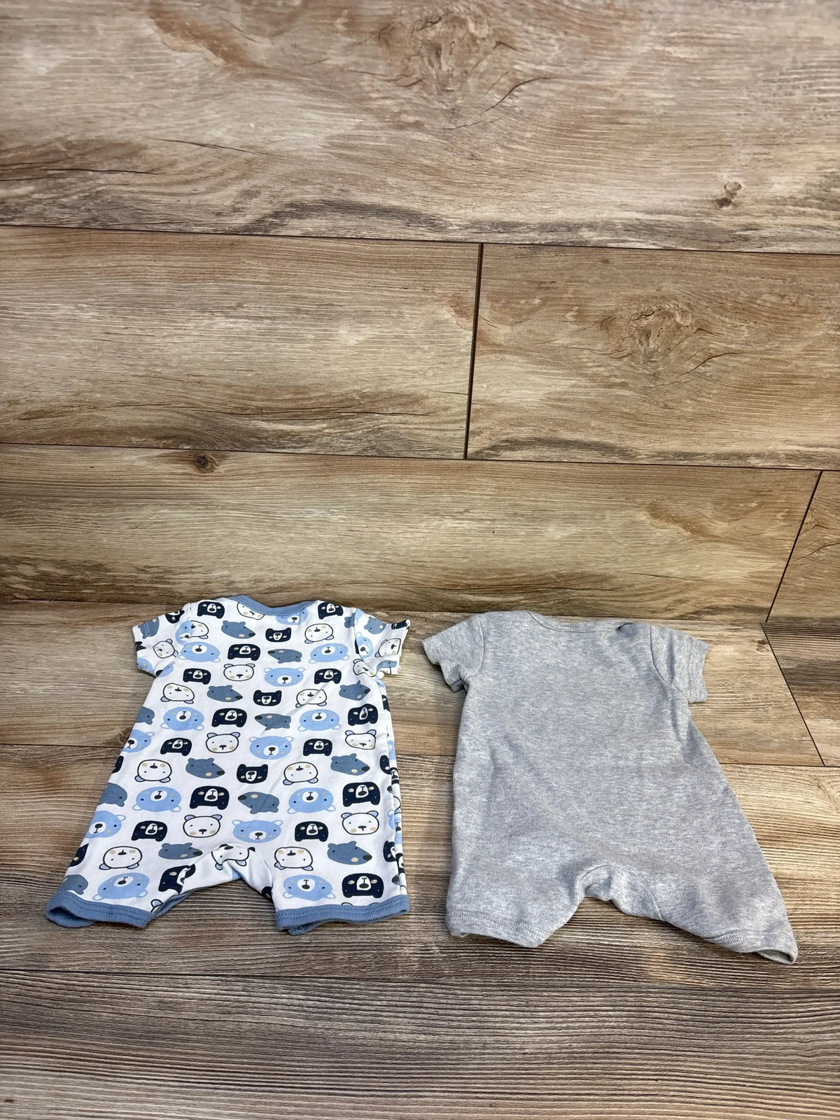 Flat lay of Payifang 2-pack shortie rompers showing one blue bear-print romper and one solid gray romper on a wood floor