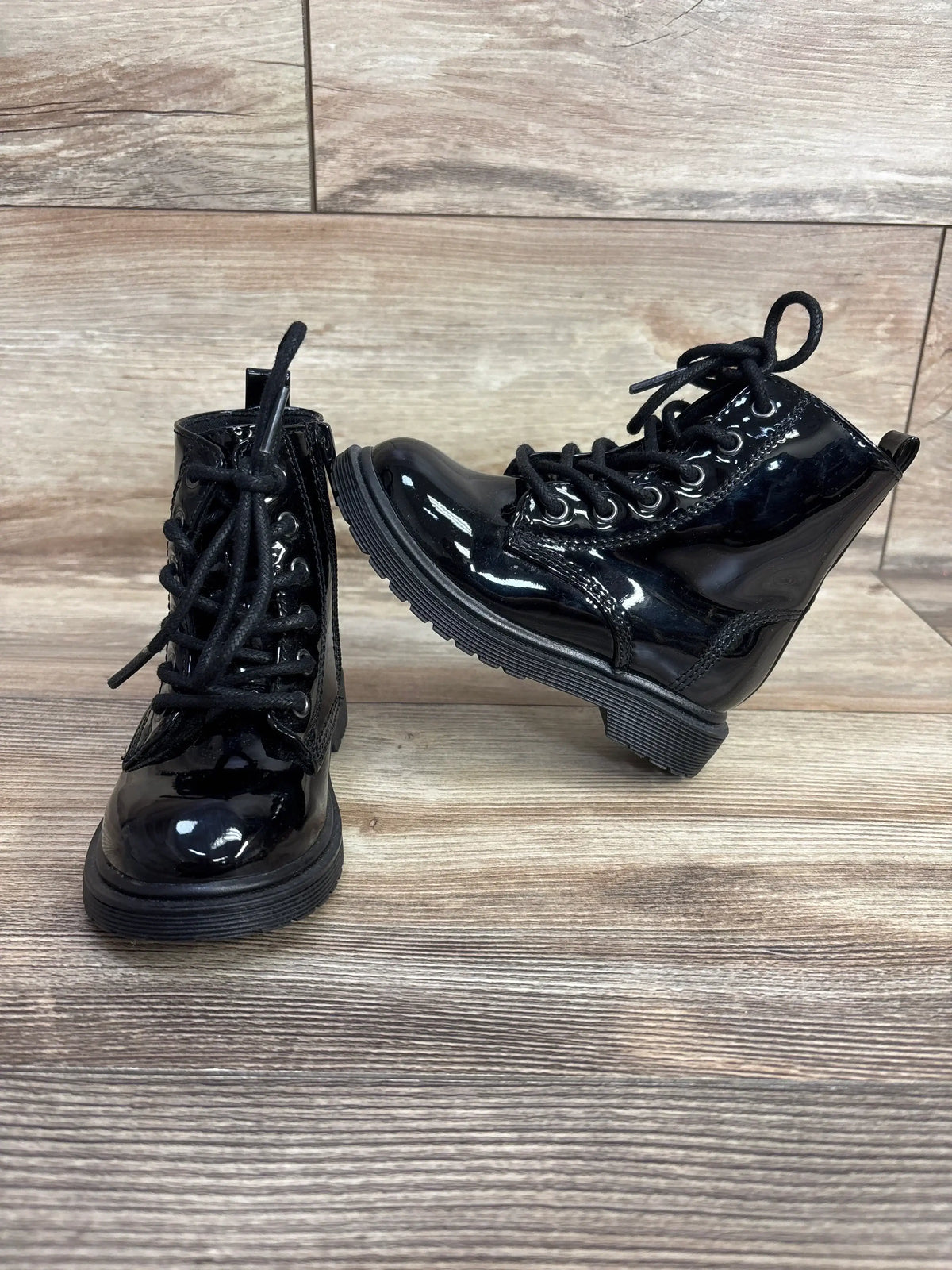 Shiny black patent leather kids lace-up boots on wood background
