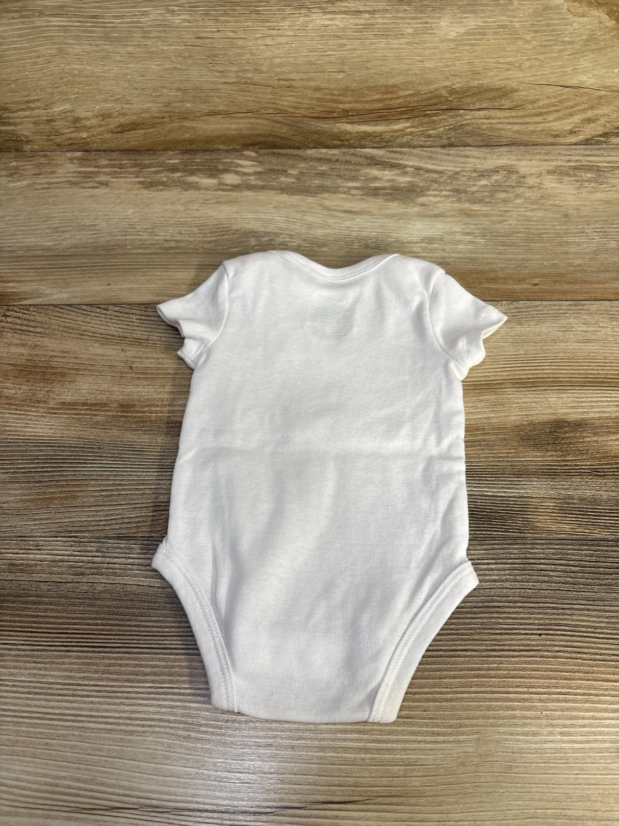 Back view of white Nike baby bodysuit, 3 months, showing short sleeves and leg openings, laid flat on wood background