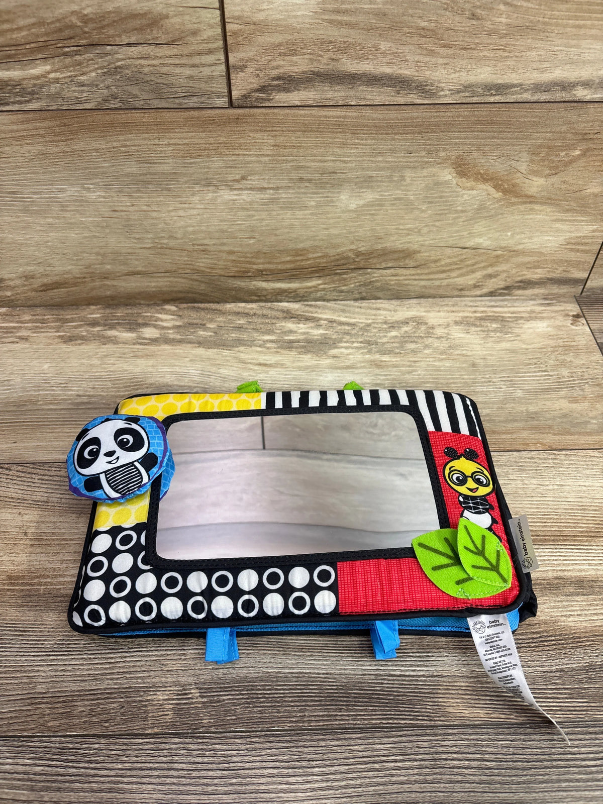 Front view of Baby Einstein Flip for Art activity mirror with high contrast patterns and fabric characters on a wood floor