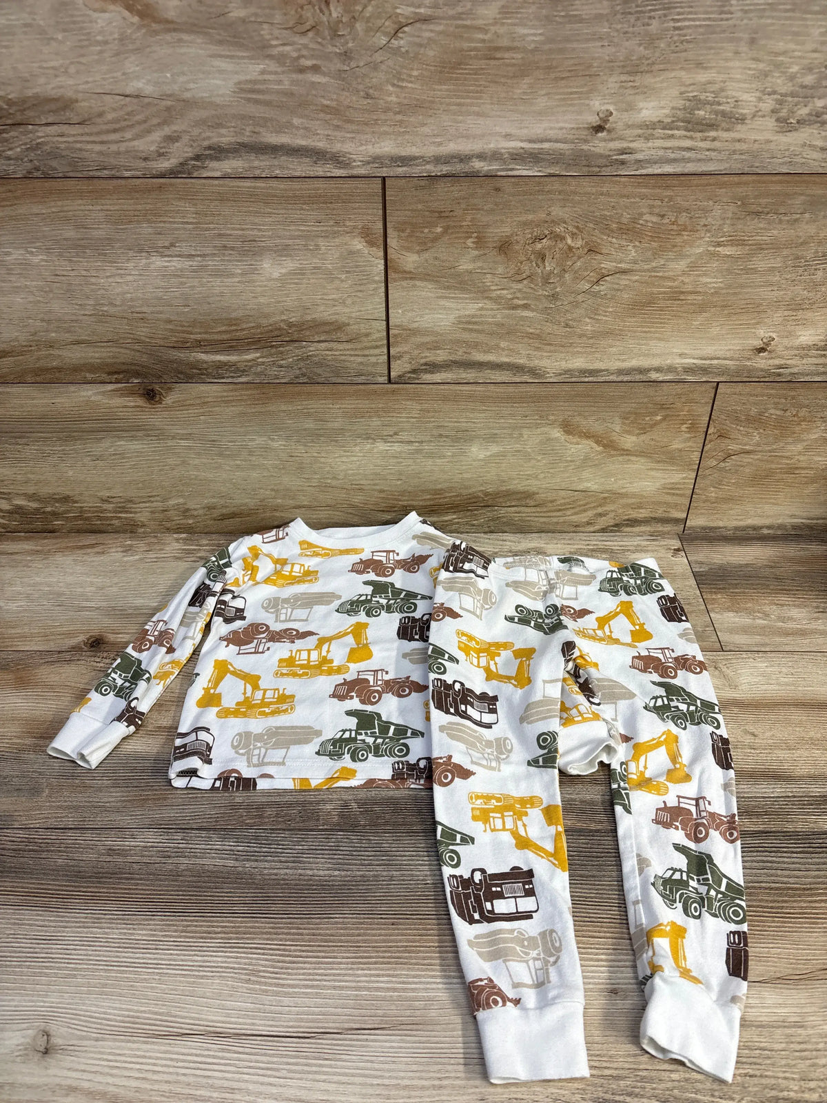 Flat lay of Carter’s 2-piece white toddler pajama set with construction vehicle print and cuffed ankles on wood background