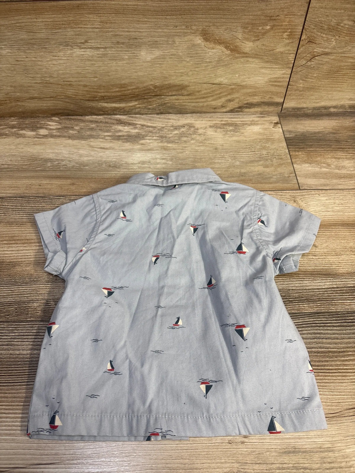 Back view of blue Modern Moments boats button up shirt in size 12 months, showing an allover sailboat print on wood floor