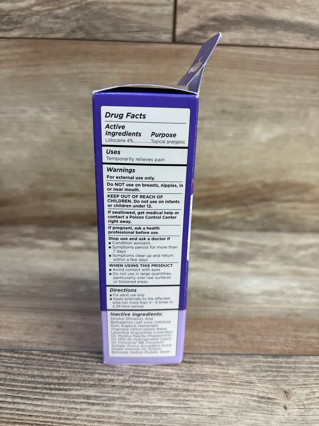 Side view of Lansinoh Postpartum Pain Relief Spray box showing drug facts panel with lidocaine 4% and warnings on wood background