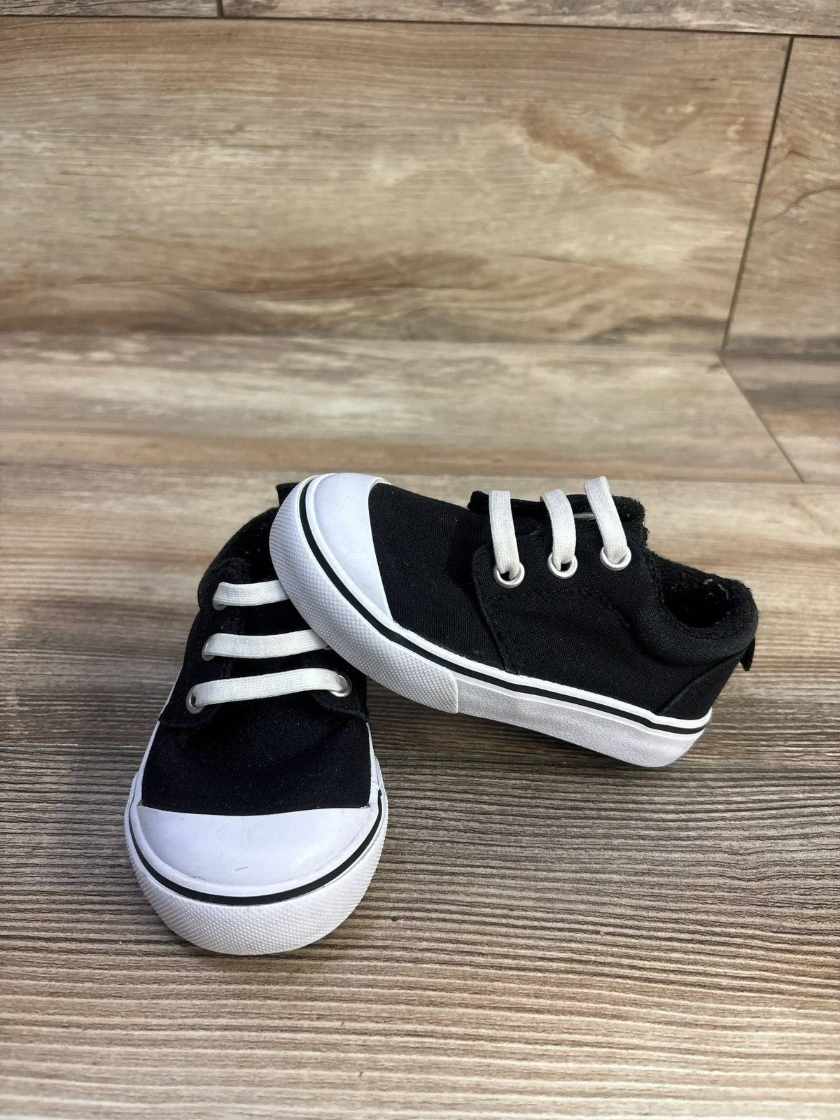 Angled side view of Wonder Nation black canvas toddler bump-toe sneakers with white rubber toe cap on wood floor