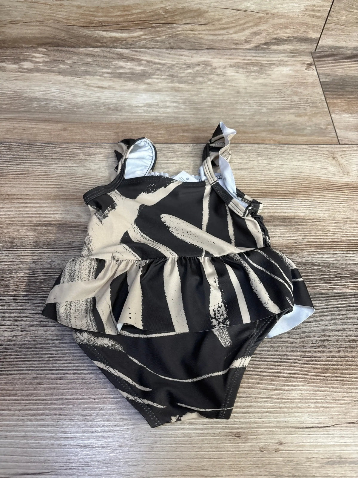 Top-down view of Carter’s one-piece zebra-print swimsuit showcasing ruffle skirt and tie shoulder straps on a wood floor