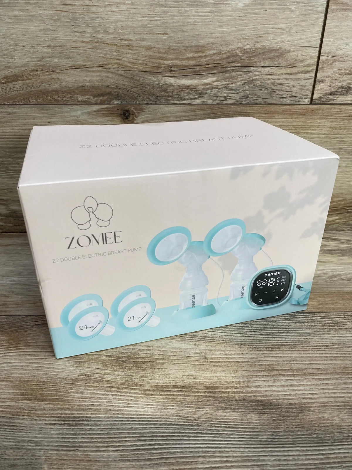 Three-quarter view of Zomee Z2 double electric breast pump box showing product image and digital control unit on wooden floor background