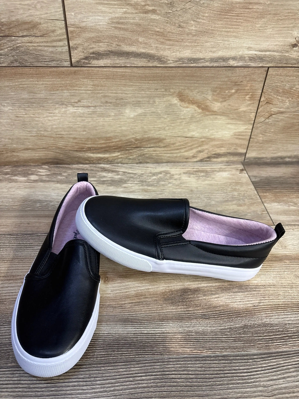 Angled top view of Cat and Jack Hailey slip on toddler sneakers showing black faux leather, white sole, pink lining on wood