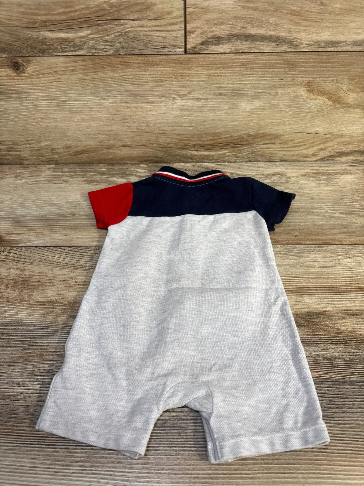 Back view of Tommy Hilfiger grey shortie romper showcasing a navy and red polo-style collar and short sleeves on wooden background