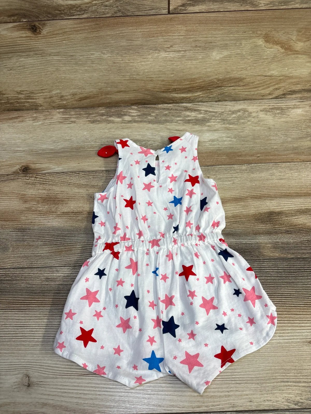 Front view of First Impressions white sleeveless romper, size 6 to 9 months, with pink, red, and blue stars on wood