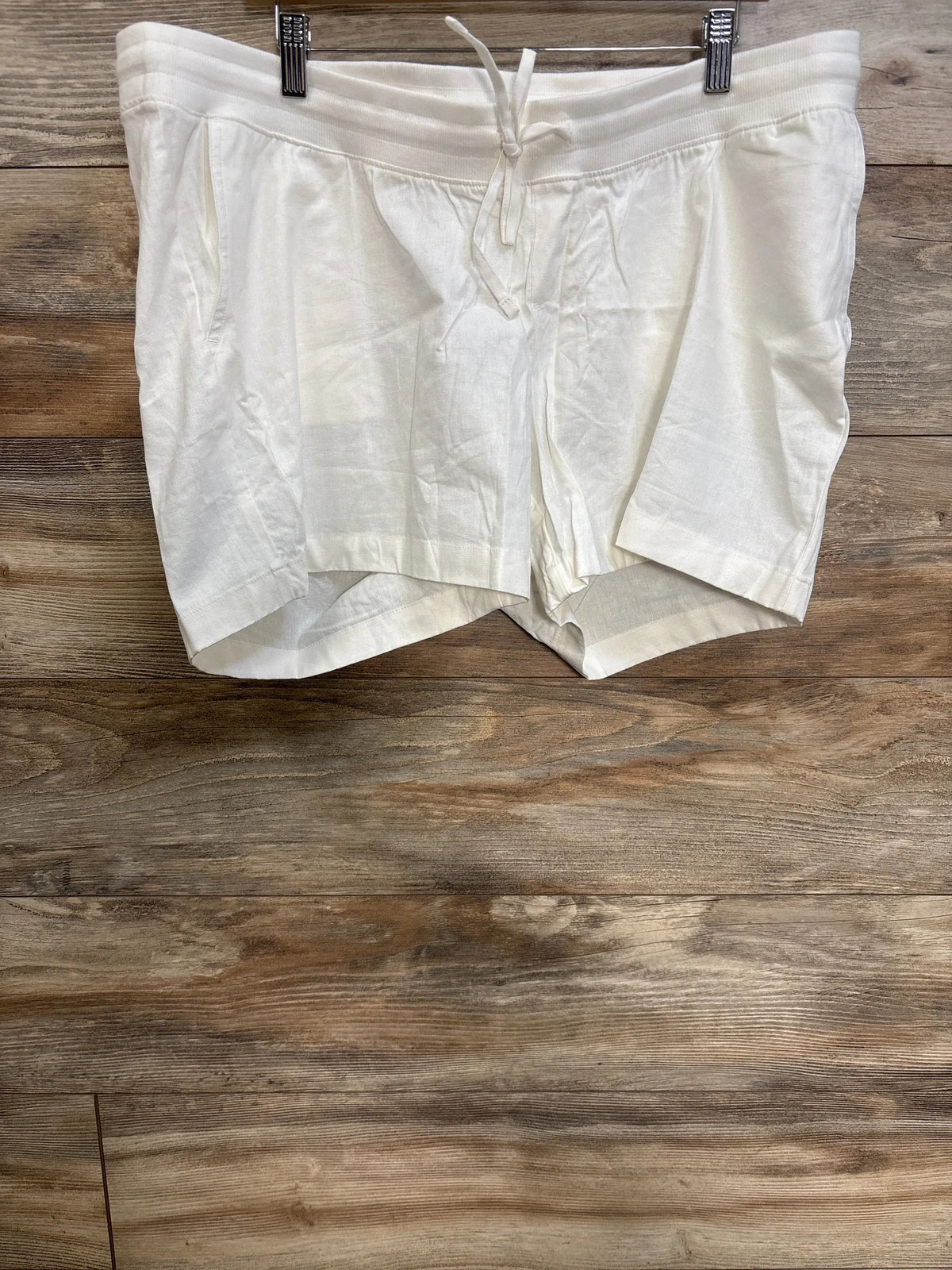 Front view of white Gap maternity linen-blend shorts showcasing under-belly elastic waist, drawcords, and slant pockets on a wood background