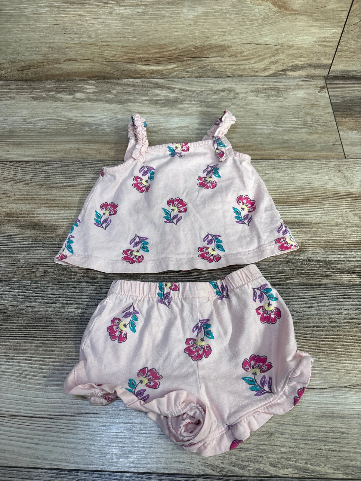 Top-down view of Carter’s pink tank top and shorts set showcasing floral print and ruffled trim on a wood-grain background