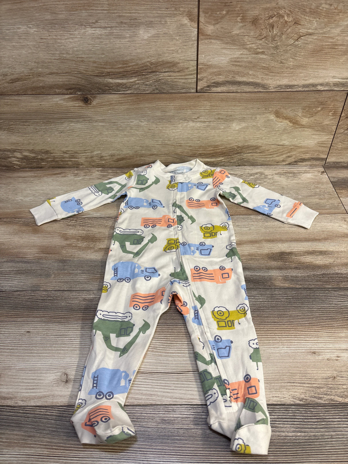 Front flat lay of Child of Mine footed sleeper showcasing center zipper and multicolored truck print with wood plank background
