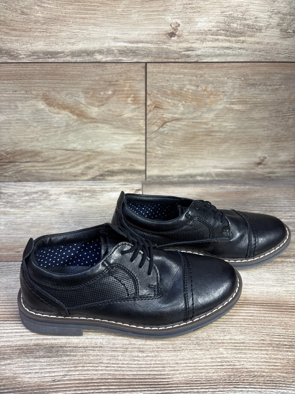 Side view of Steve Madden Toliverr cap-toe Oxford shoes with cap-toe stitch and white welt on wood floor