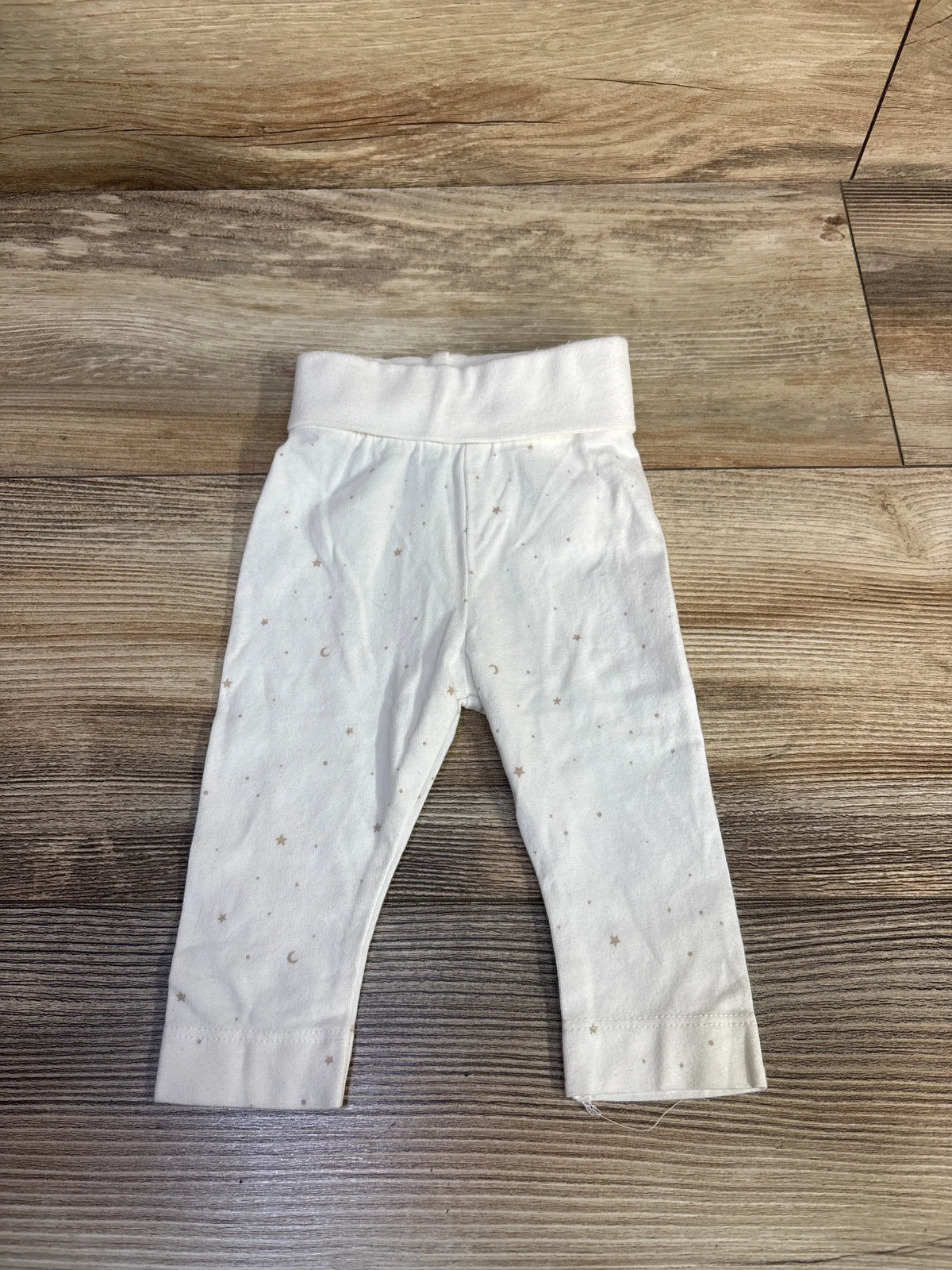 Front view of white H&M newborn pants showcasing foldover waistband, cuffed hems, and star-and-moon pattern on a wooden floor
