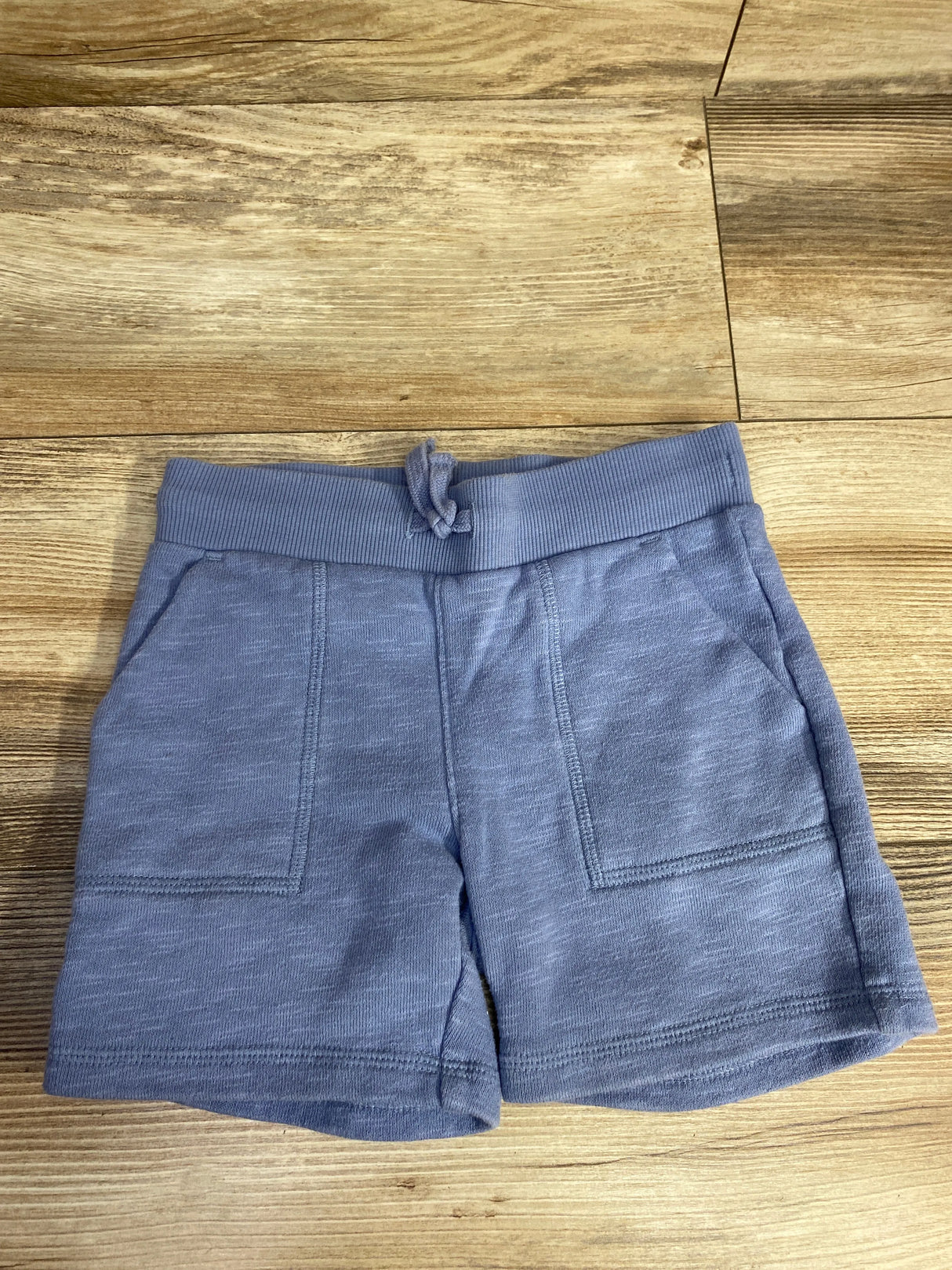 Blue toddler shorts with front pockets and drawstring waist on wooden floor