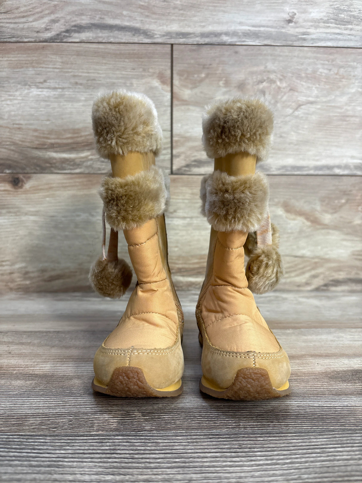 Tan fur lined winter boots with pom poms on wood background, cozy footwear style