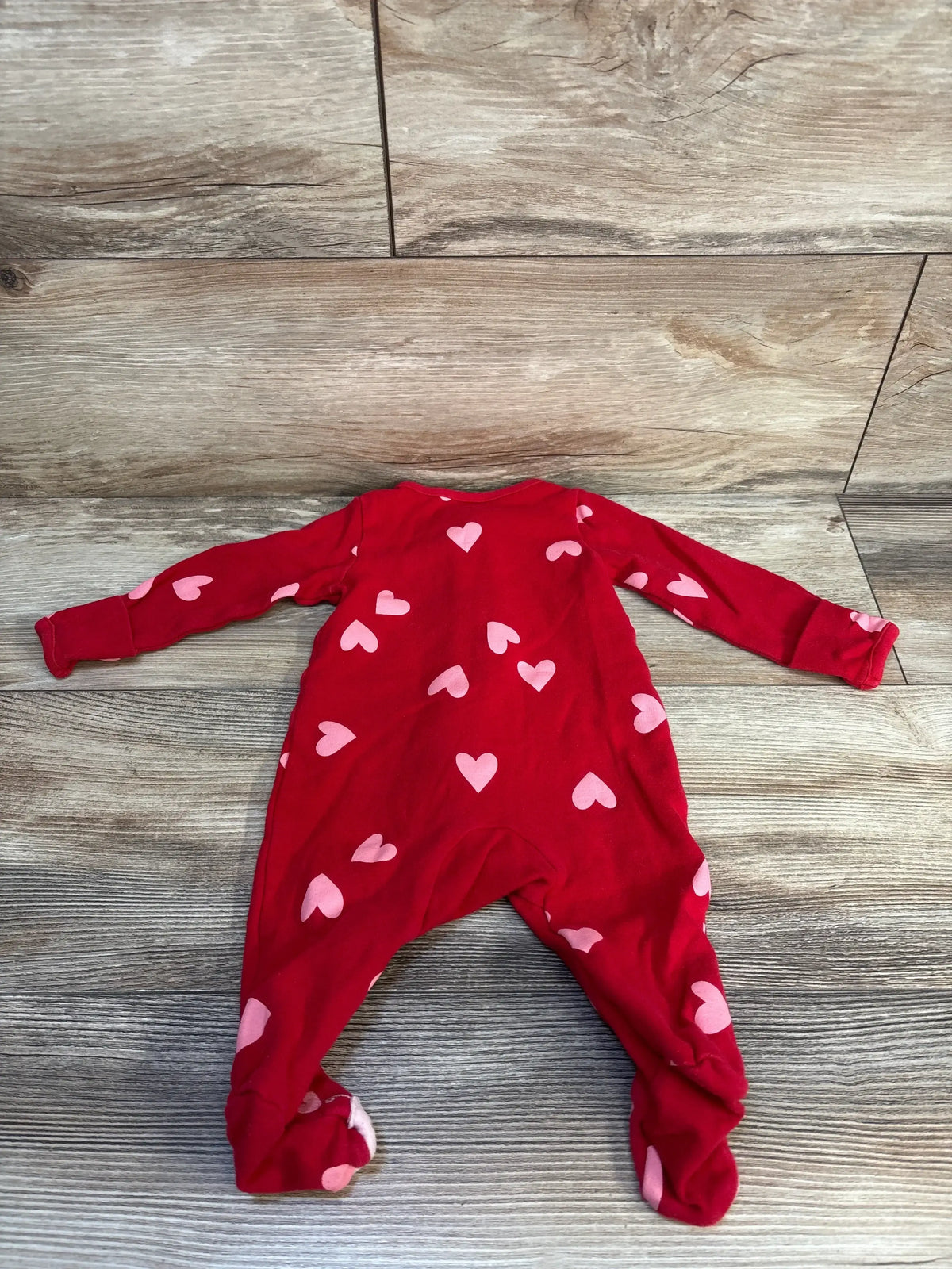 Red baby sleeper with pink heart pattern on wood background