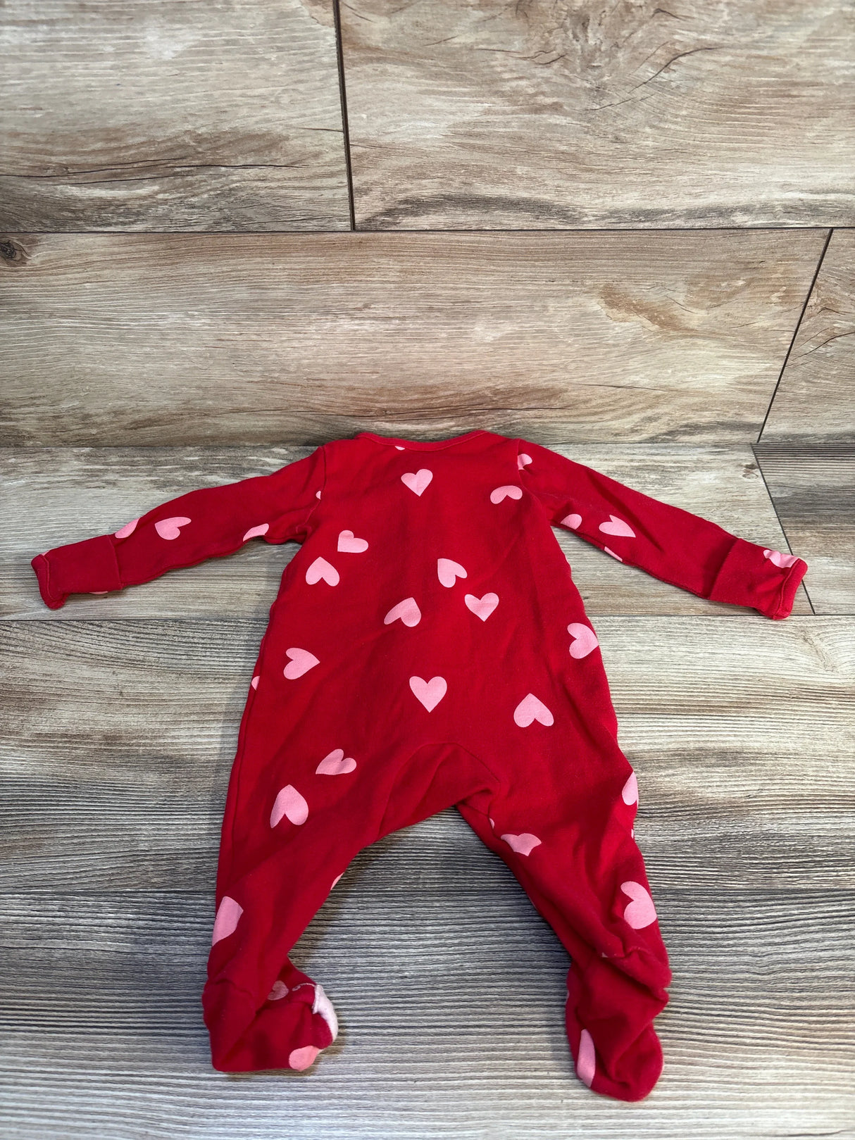 Red baby sleeper with pink heart pattern on wood background