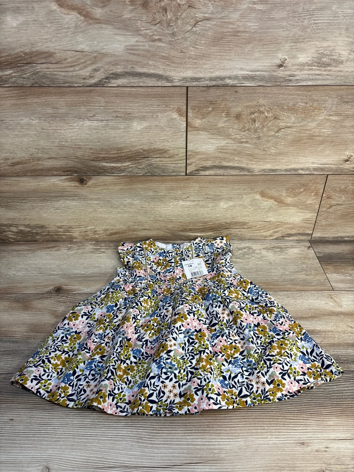 Infant floral dress with ruffled sleeves and colorful flower print on wood background