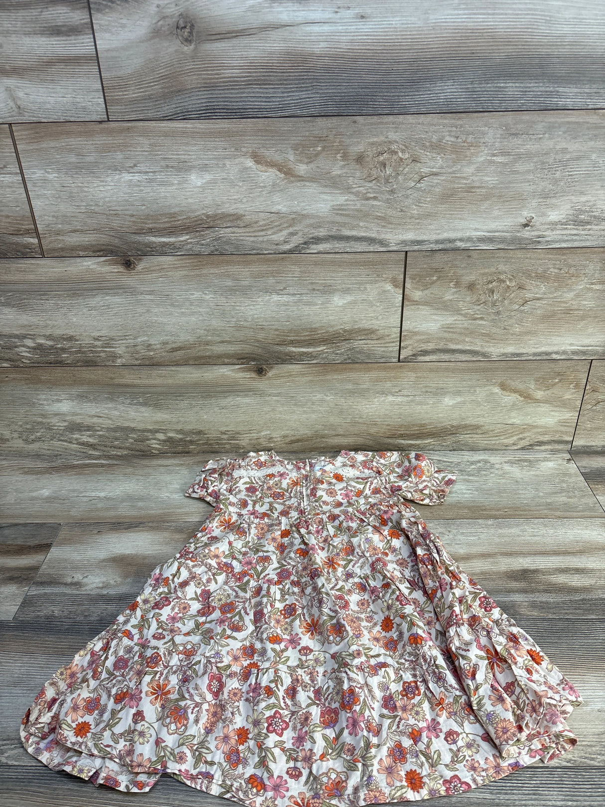 Flat lay of girls' ivory floral swing dress size 5T showing short ruffle sleeves and tiered skirt on light wood background