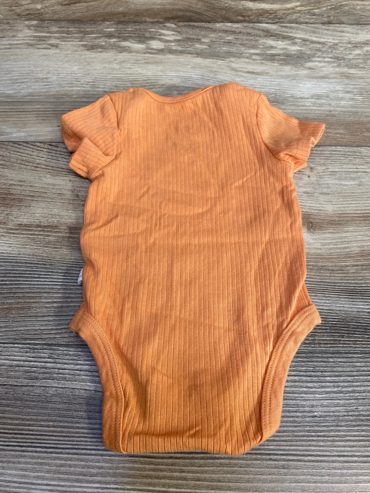 Top-down view of orange Mori ribbed bodysuit with short sleeves, lap shoulder and three-snap crotch on wood background
