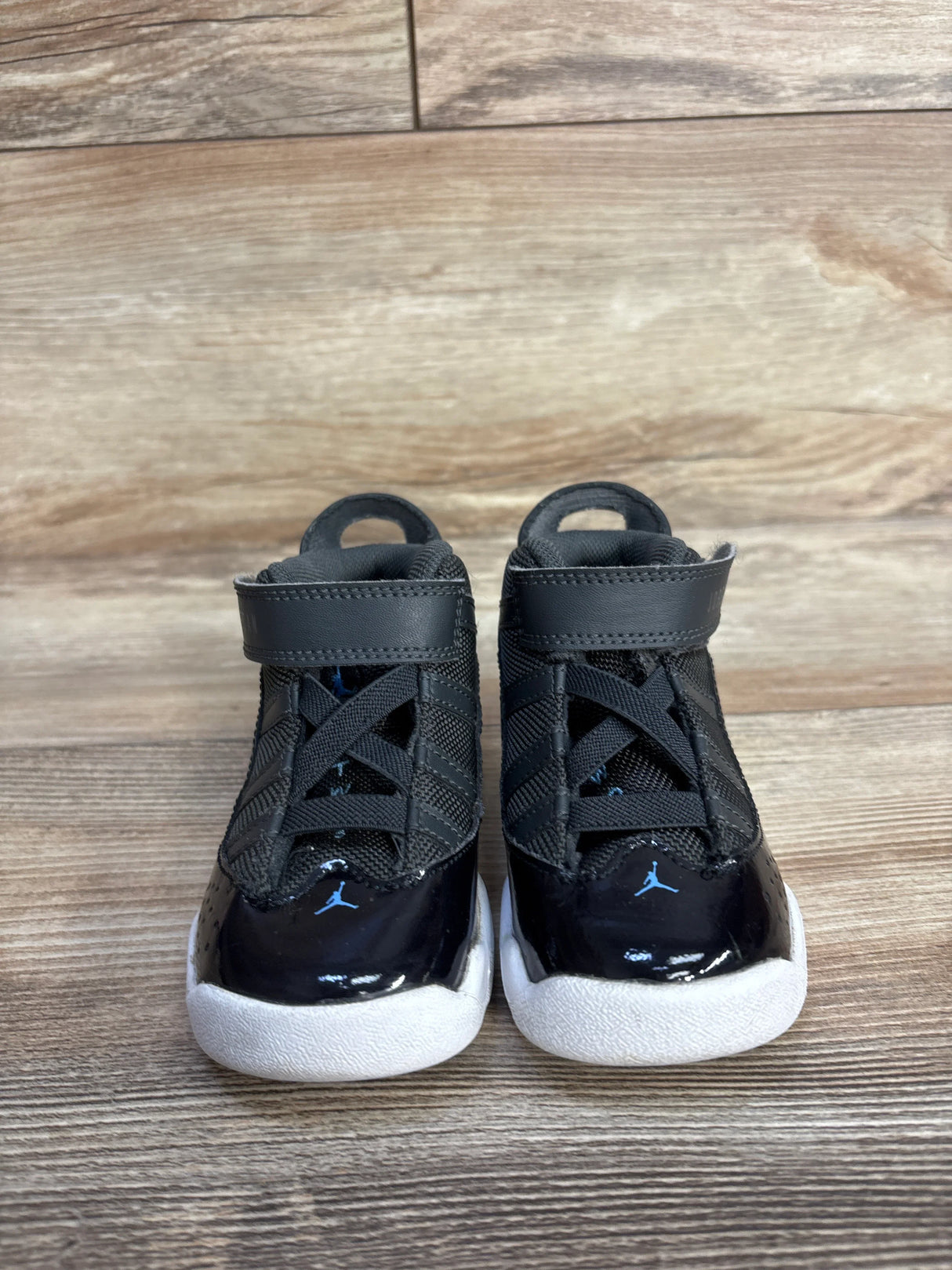 Black toddler Jordan sneakers with blue Jumpman logo on wooden floor
