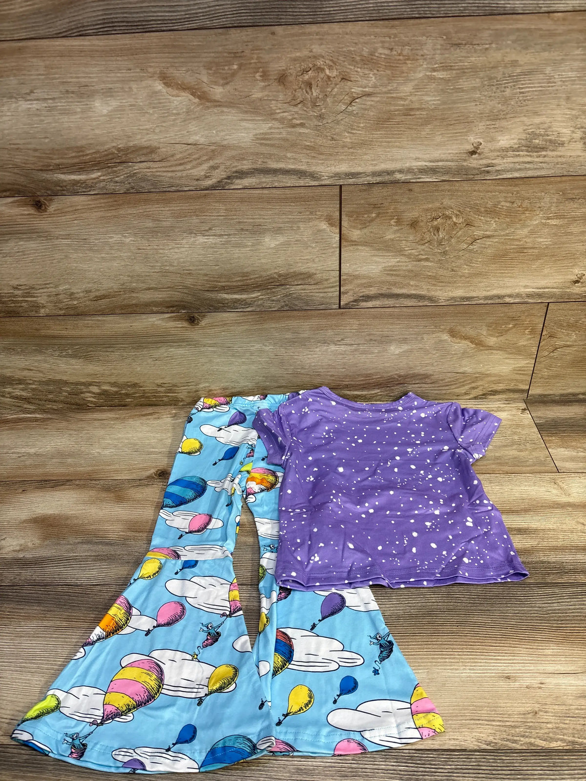 Flat lay of Dr Seuss two-piece toddler set with purple splatter tee and blue hot air balloon bell-bottoms on wood background