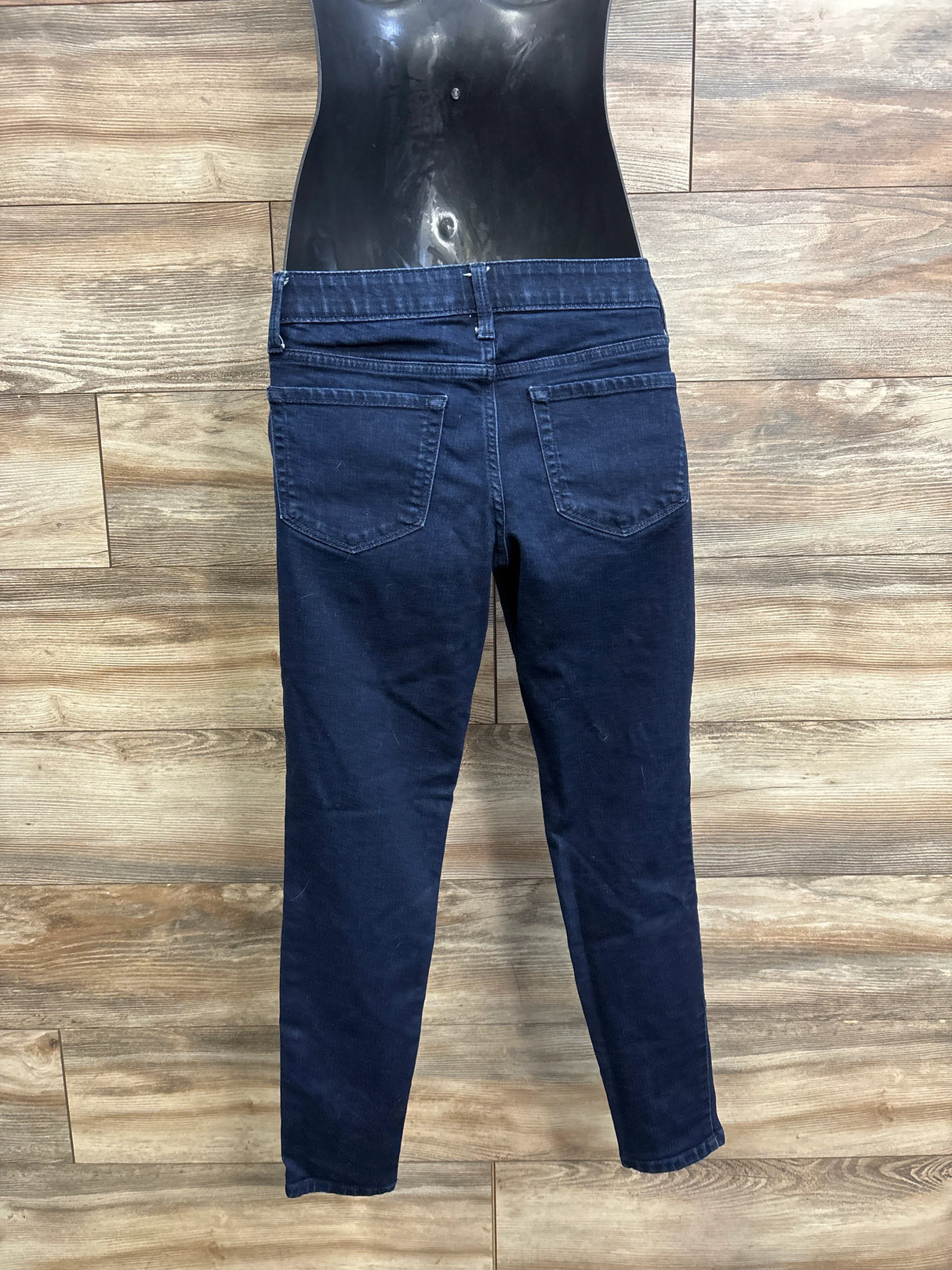 Back view of blue maternity jeggings showing side-panel waistband, back pockets, and tapered legs against wood plank background