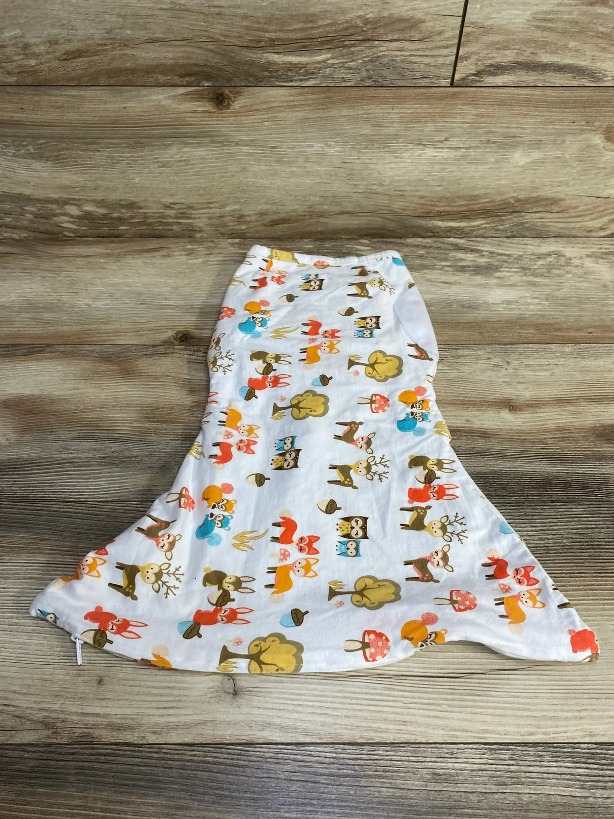 Top-down view of newborn zippy swaddle showing woodland animal print with foxes, owls, deer and mushrooms on wood plank background