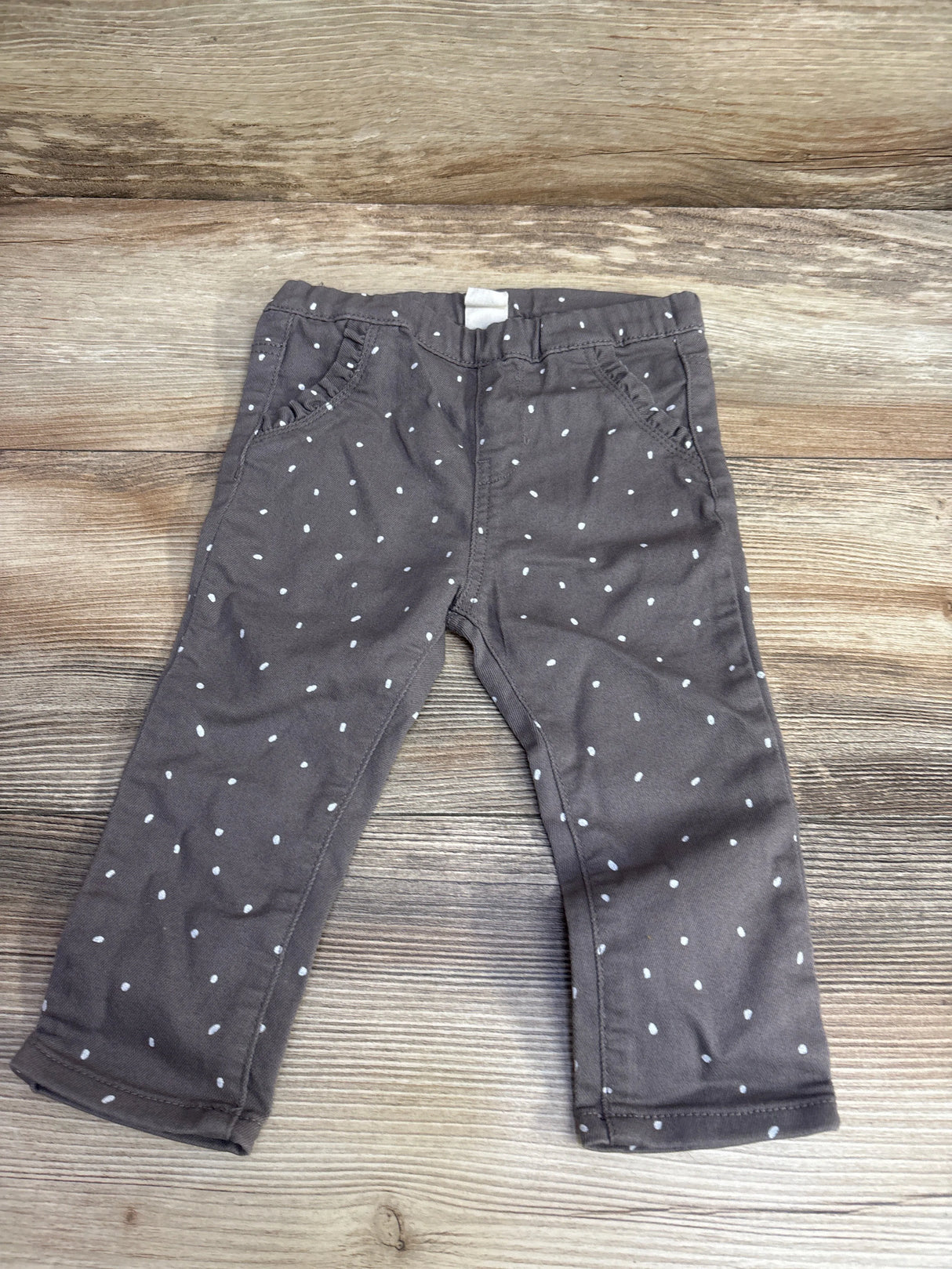 Children's gray pants with white polka dots laid flat on wooden surface, kids clothing