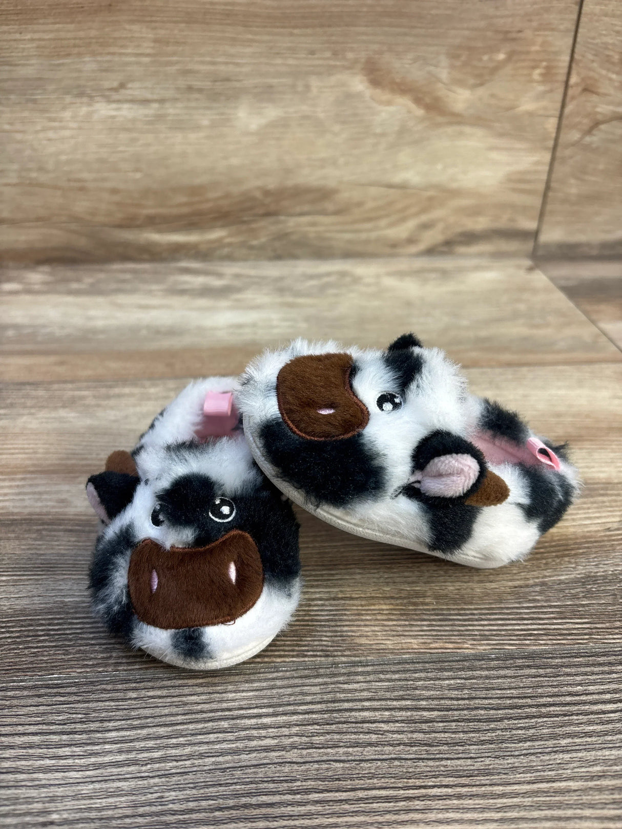 Plush black and white cow baby booties with cute faces on wood background