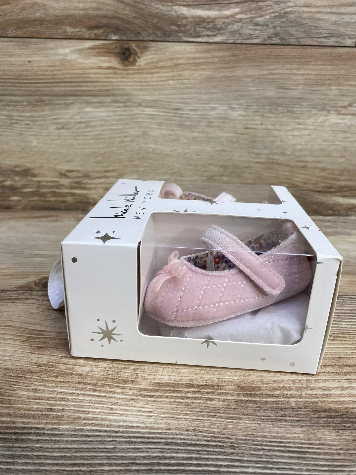 Pink baby girl crib shoes with bow in box on wood background, newborn footwear gift