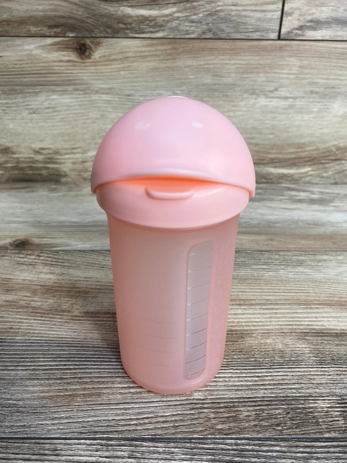 Front view of pink plastic baby formula shaker bottle with dome lid measurement window and ounce scale on wood plank floor