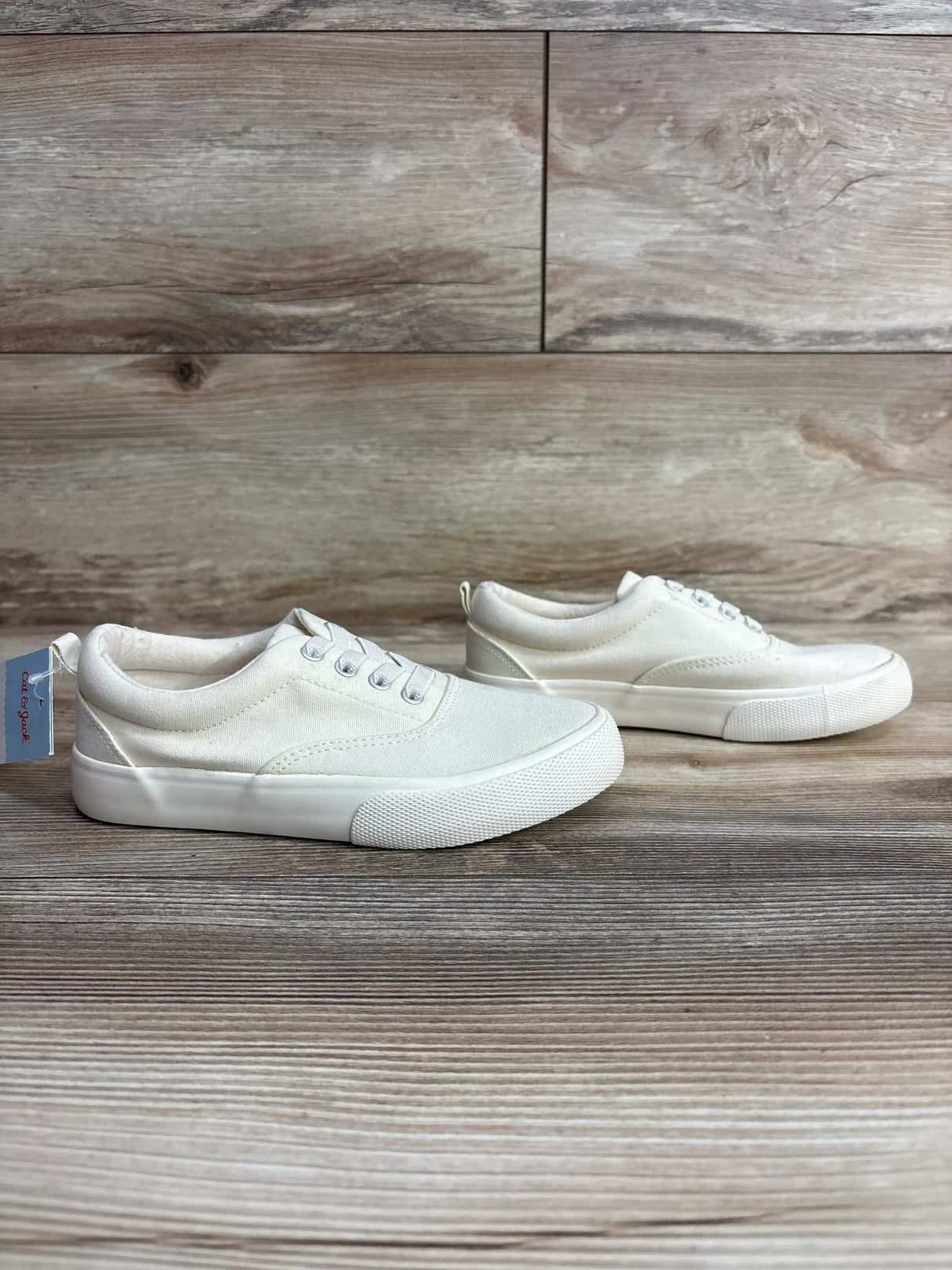 White canvas kids sneakers with laces on wood background, gently used condition