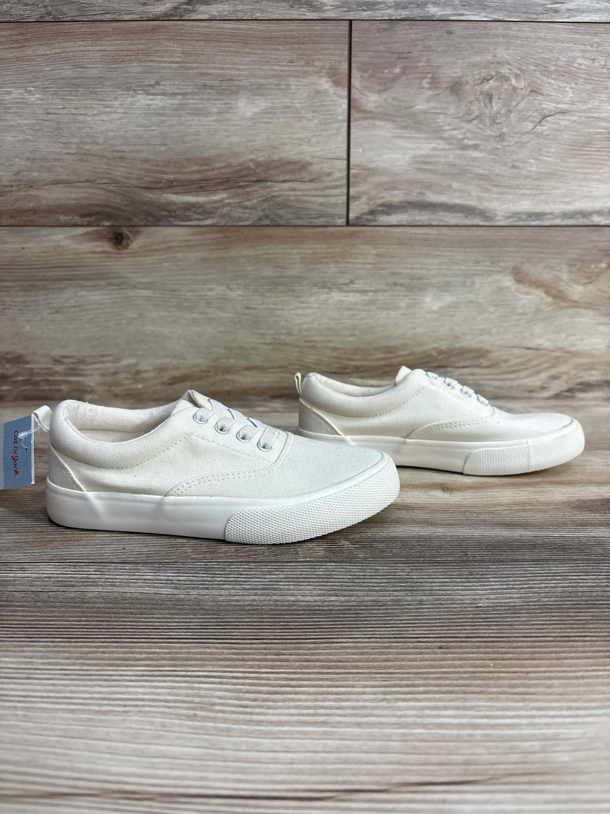 Side view of Cat & Jack Tyler slip-on kids sneakers in off-white showing canvas upper and white rubber sole on wood background, size 13C
