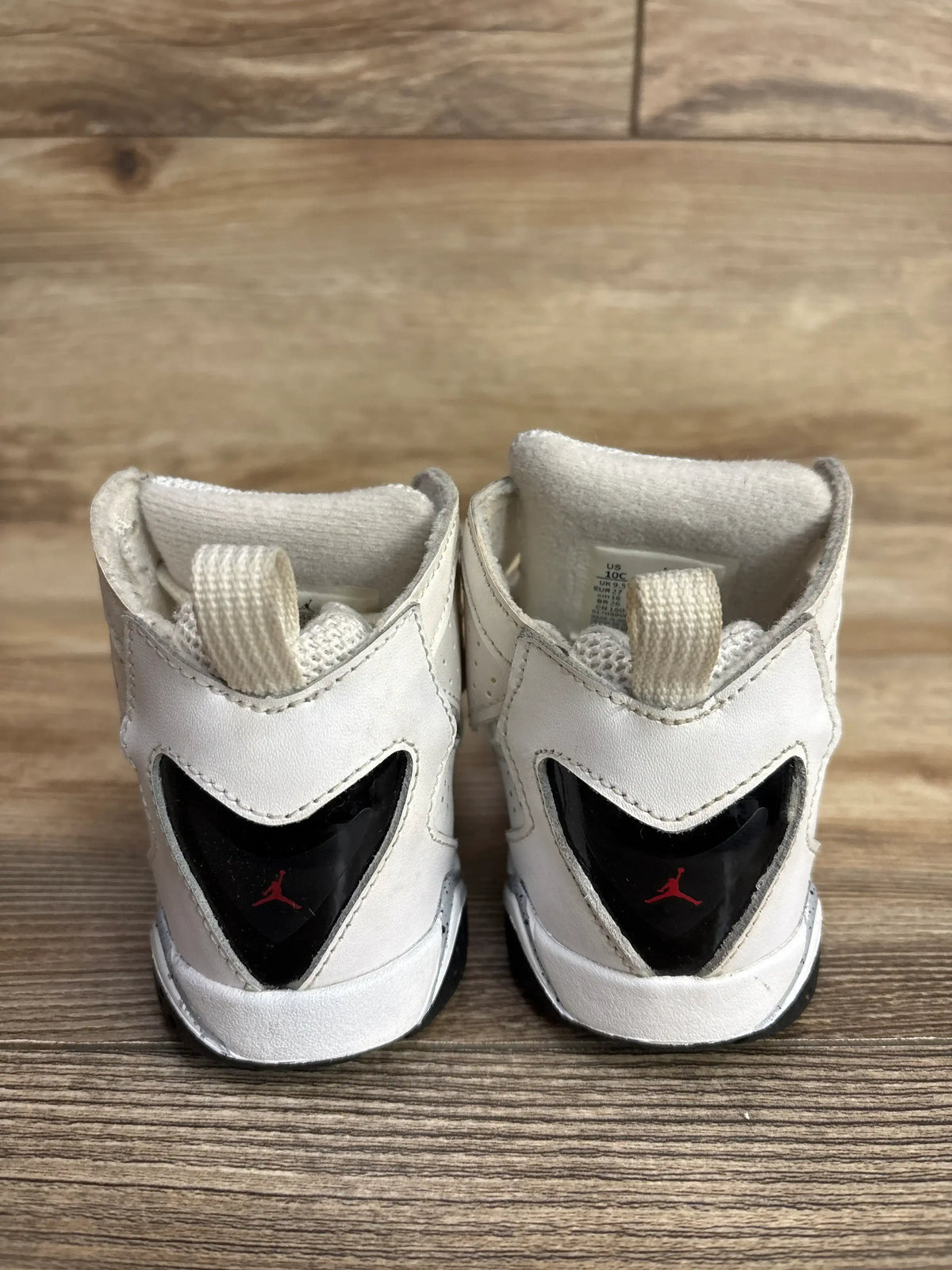 Pair of white toddler Air Jordan sneakers with black and red logo, displayed on wooden surface