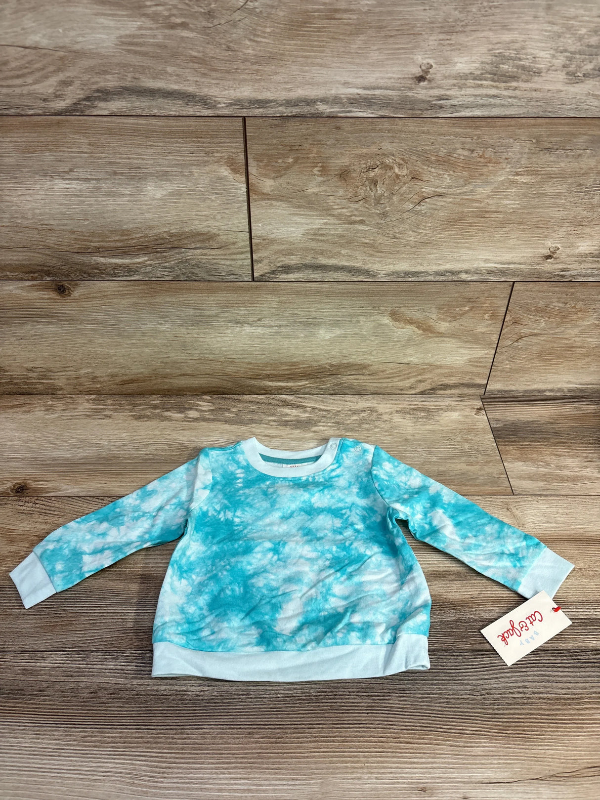 Blue tie-dye long sleeve baby sweatshirt with tag on wooden background