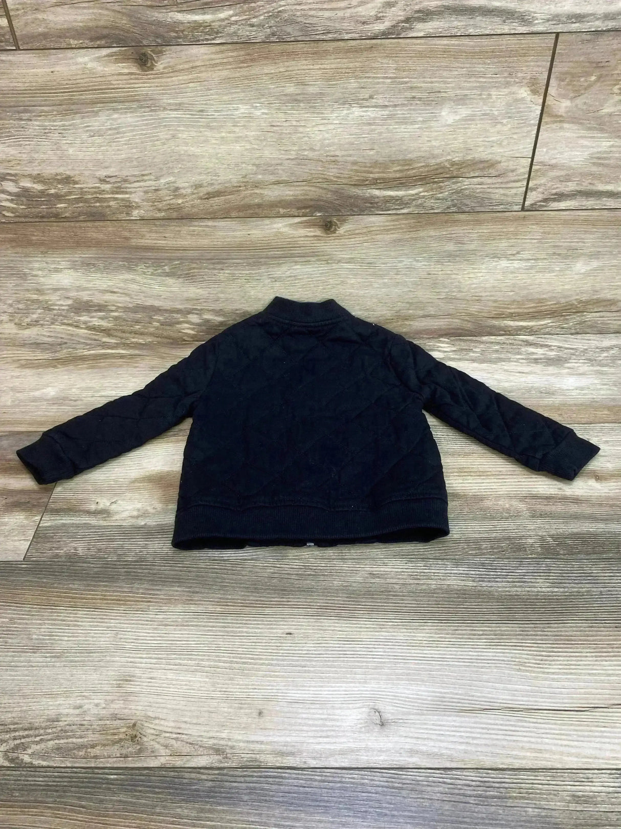Back view of Wonder Nation quilted jacket in black size 24m showcasing stand collar and ribbed cuffs on wood plank floor