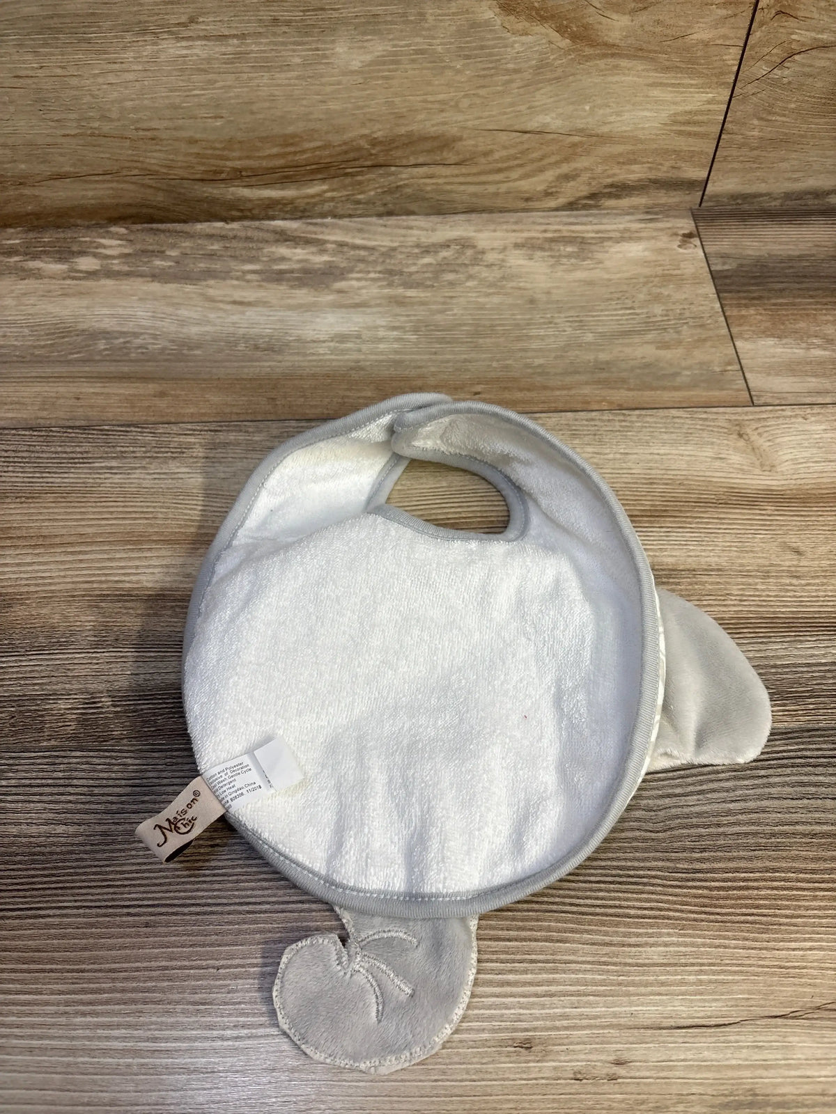 Top-down view of Maison Chic Emerson elephant bib with white terry front, gray trim and plush elephant ears on wood floor