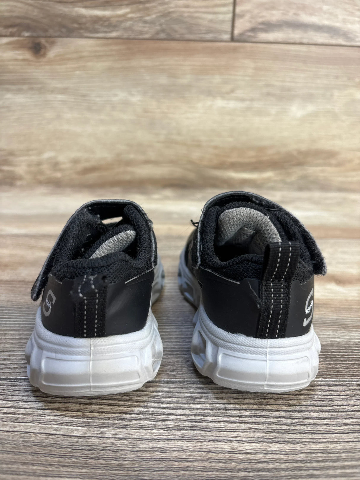 Back view of black and white kids athletic sneakers on wooden floor