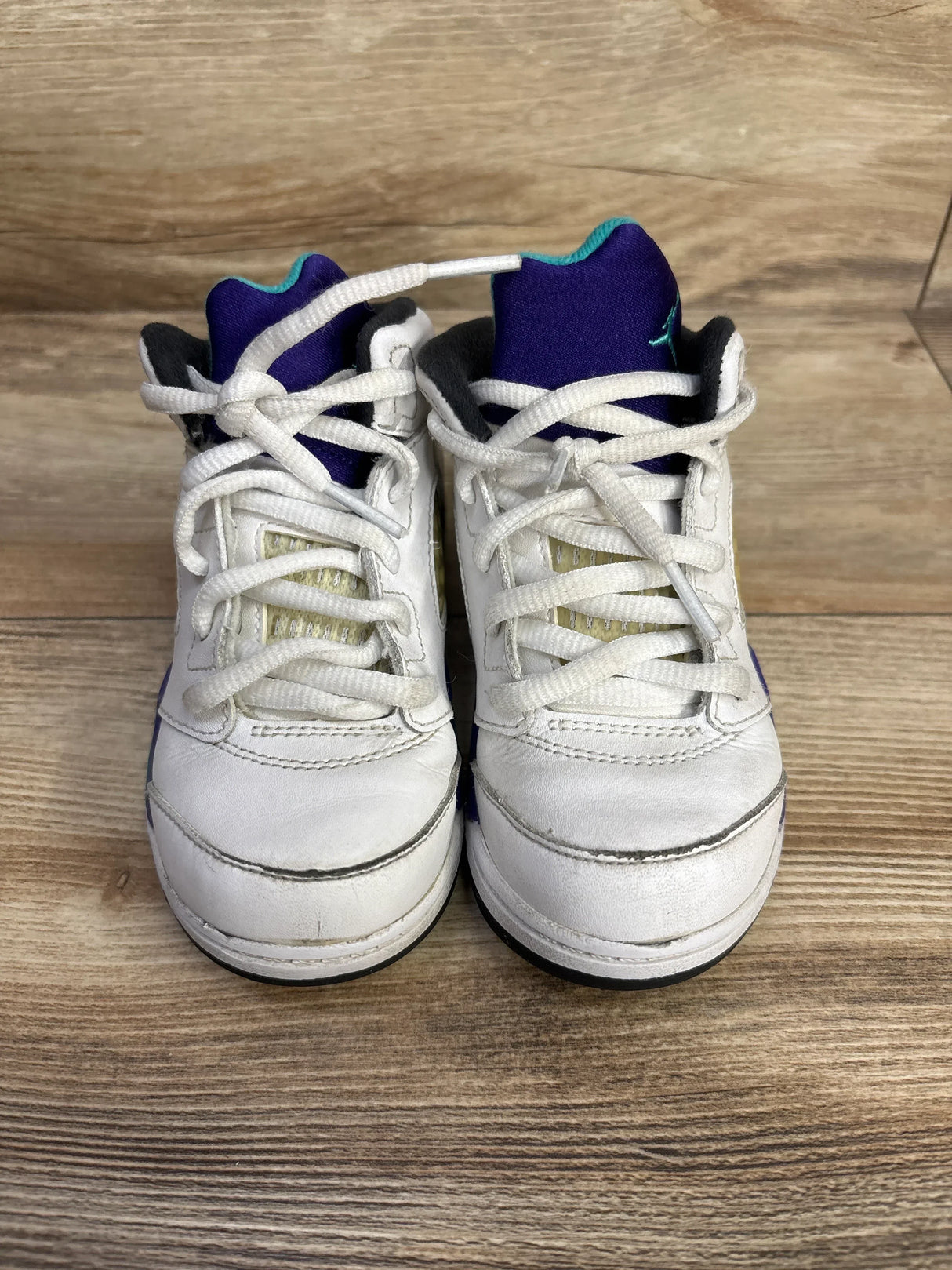 Front view of Air Jordan 5 Retro TD Grape toddler sneakers showing white leather uppers, purple tongues with teal accents and white laces on a wooden floor