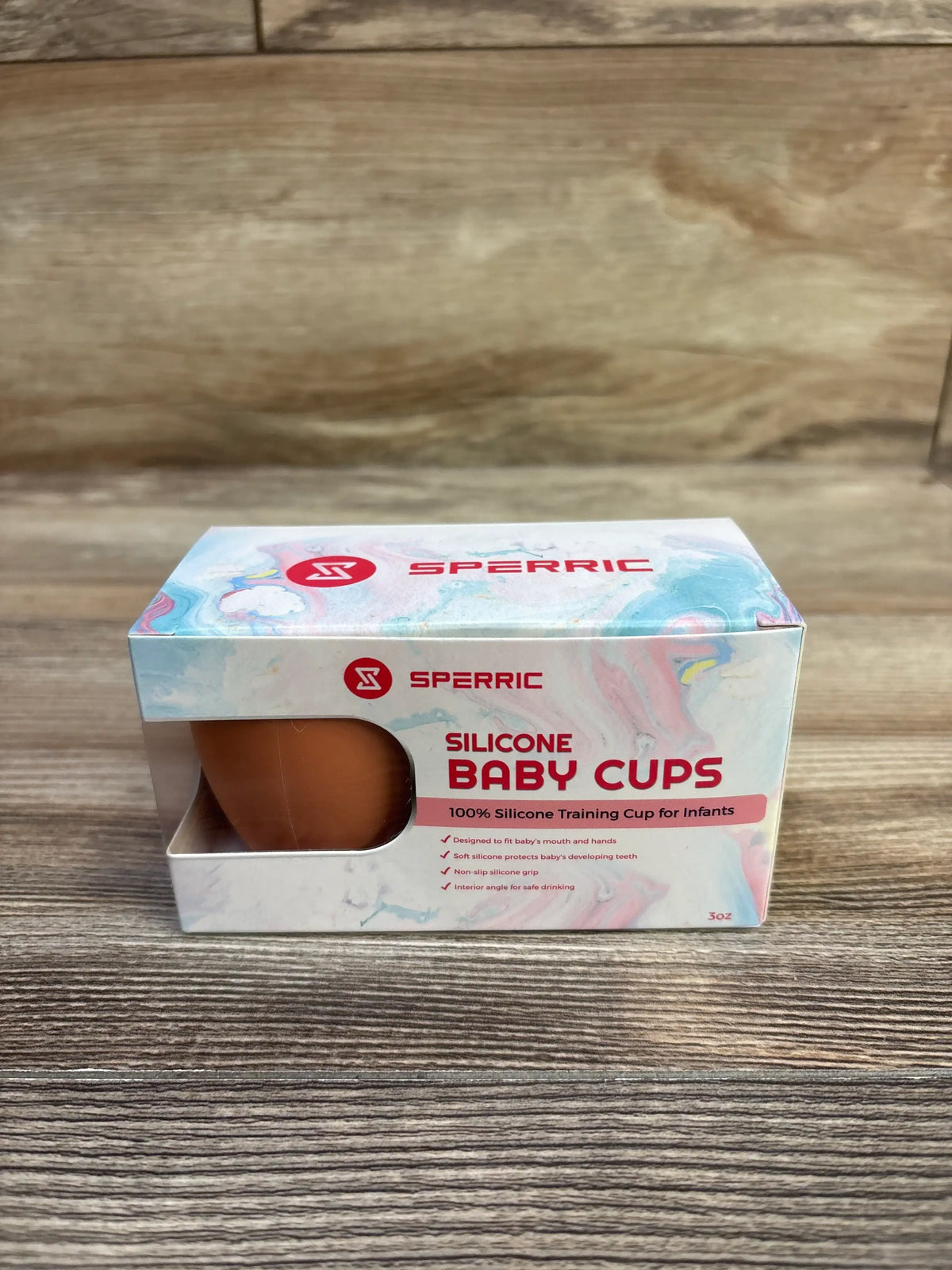 Front view of Sperric silicone baby cups 3 oz two-pack box showcasing a brown cup visible through the front window on a wood tabletop